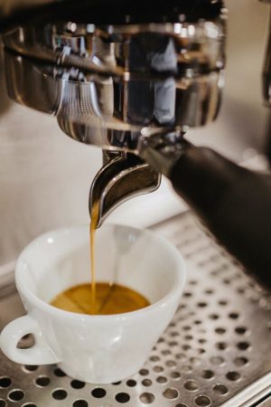 Nahaufnahme der Siebträgermaschine während frisch gebrühter Espresso in ein kleines Espresso-Tässchen fließt.