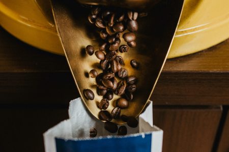 Kaffeebohnen fallen aus der Öffnung einer Kaffeeschütte in eine Aromatüte.Kaffeebohnen fallen aus der Öffnung einer Kaffeeschütte in eine Aromatüte.